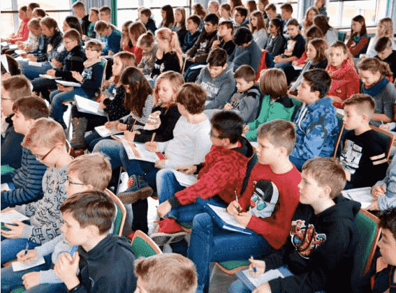Schülerinnen und Schüler sitzen in der Aula