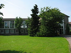 Schulgebäude des Woeste-Gymnasiums hinter einer Rasenfläche mit Bäumen